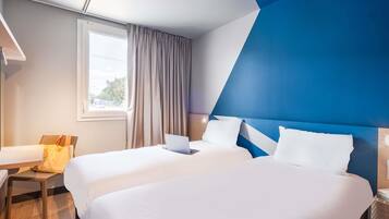 Habitación de hotel con dos camas, un escritorio, una silla, un ventanal y una pared de acento azul.