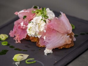Prato com peixe rosa, queijo branco e guarnição verde sobre um prato escuro.