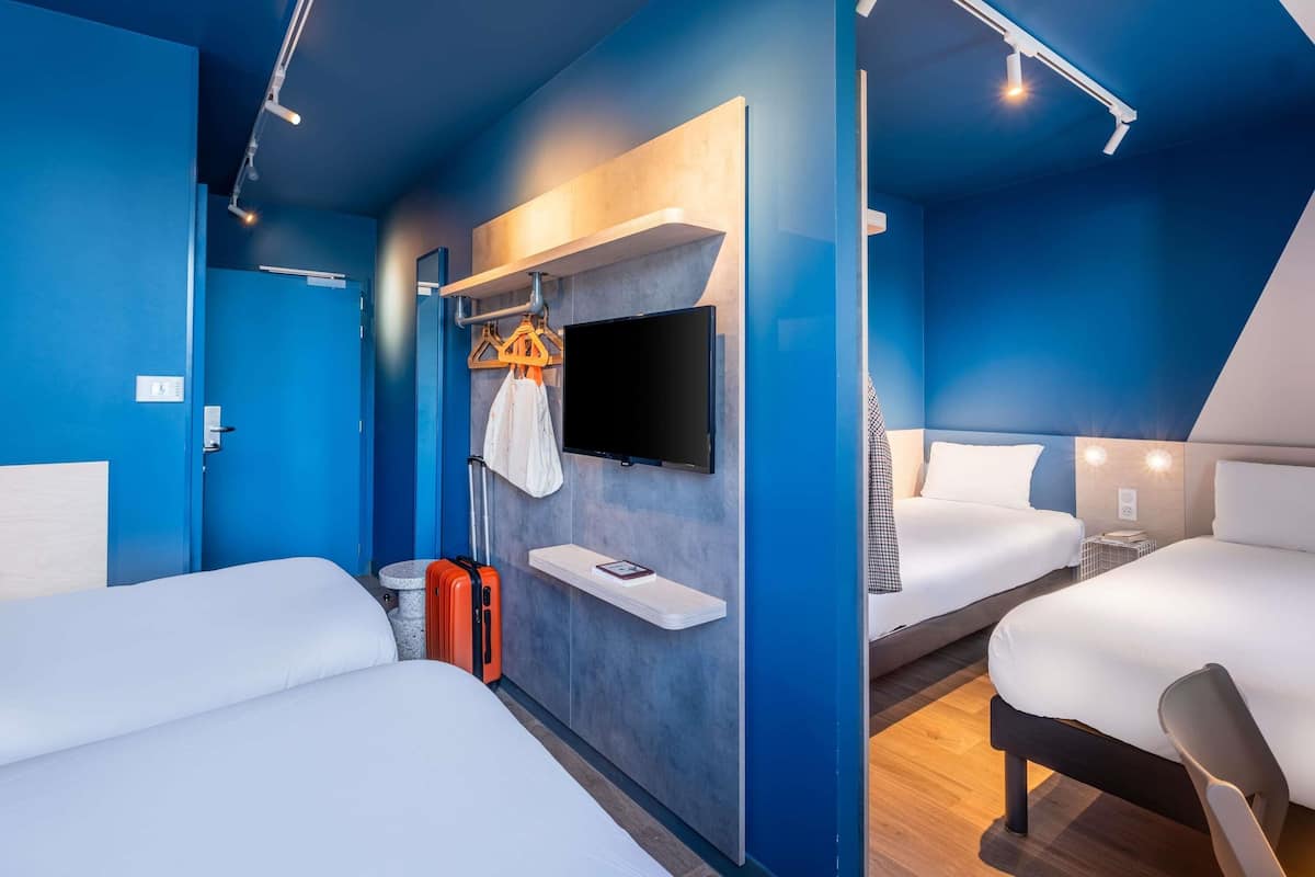 Une chambre d’hôtel moderne avec deux lits, un téléviseur à écran plat, un petit bureau et une valise.
