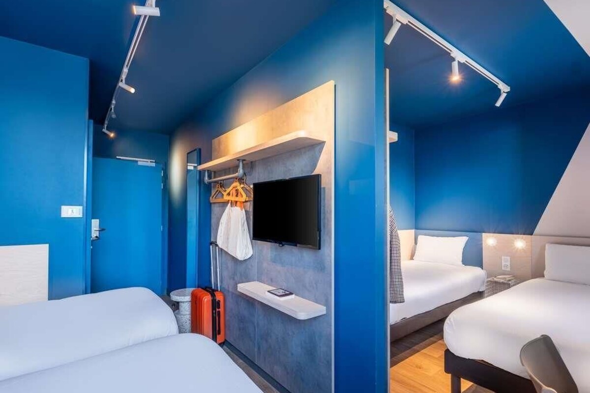 Habitación de hotel con dos camas, un televisor montado en la pared y una maleta en el suelo.