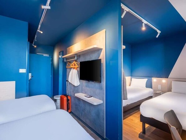 Habitación de hotel con dos camas, un televisor montado en la pared y una maleta en el suelo.