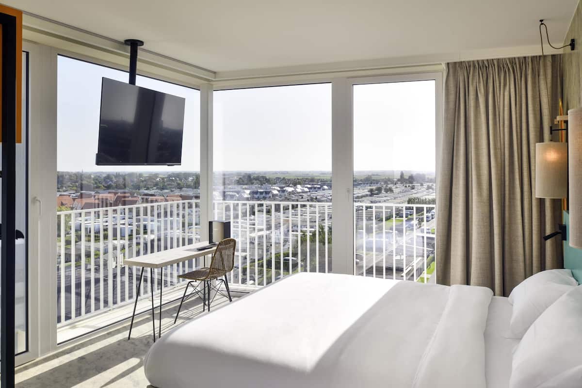 Une chambre d’hôtel avec un lit, une télévision, un balcon avec une table et une chaise, et une vue sur la ville.
