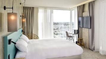 Una habitación de hotel moderna con una cama grande, un escritorio con una silla, un televisor y vistas a la ciudad.
