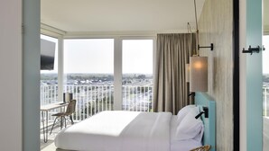 A bedroom with a large bed, a chair, a TV, and a balcony with a city view. - Ibis Styles Bredene  (Bredene)
