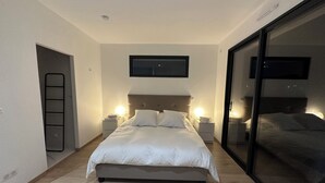 A modern bedroom with a large bed, bedside lamps, a sliding glass door, and a framed picture on the wall.