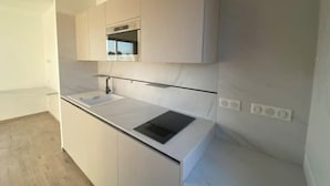 A modern kitchen with white cabinetry, a black countertop, and a built-in oven.