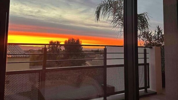A balcony with a view of a sunset over a residential area.