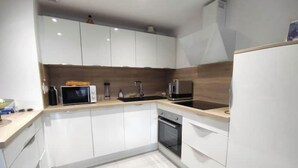 Une cuisine moderne avec des meubles blancs, un four à micro-ondes, une machine à café et une cuisinière.