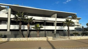 Un immeuble moderne à plusieurs étages, doté d’un toit plat et de balcons. Des palmiers sont plantés devant.