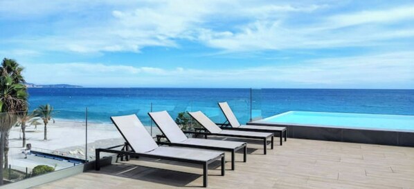 A rooftop pool area with lounge chairs facing the ocean.