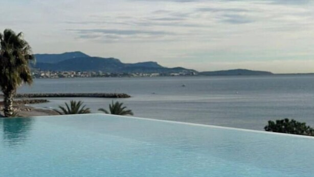 Une magnifique piscine à débordement d’un bleu profond, offrant une vue sur la mer et les montagnes lointaines.