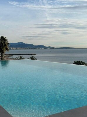 A clear blue infinity pool with a view of the sea and distant mountains. - Résidence Pearl Beach - Piscine sur le Toit (Villeneuve-Loubet)