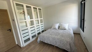 Quarto com cama, guarda-roupa de portas de vidro e janela.