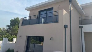 Um edifício moderno de dois andares com varanda no andar superior, janelas amplas e telhado plano.