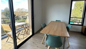 Uma sala de jantar moderna com mesa de madeira e cadeiras cor turquesa, grandes janelas e vista para o exterior.