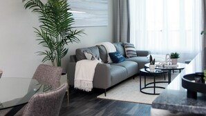 Una sala de estar moderna con un sofá gris, una mesa de centro, una mesa de comedor con sillas y una planta grande.