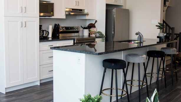 Una cocina moderna con gabinetes blancos, electrodomésticos de acero inoxidable y una isla central con taburetes de bar.