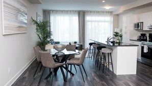 Una cocina moderna con una isla central, taburetes de bar y un comedor con mesa y sillas de vidrio.
