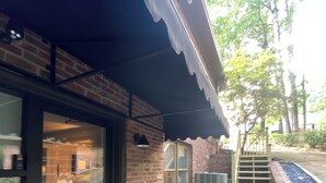 A brick building with a glass door, a small outdoor seating area with a table and plants, and a staircase leading to a higher level. - Trilith Studios Area Lakefront  (Sharpsburg)