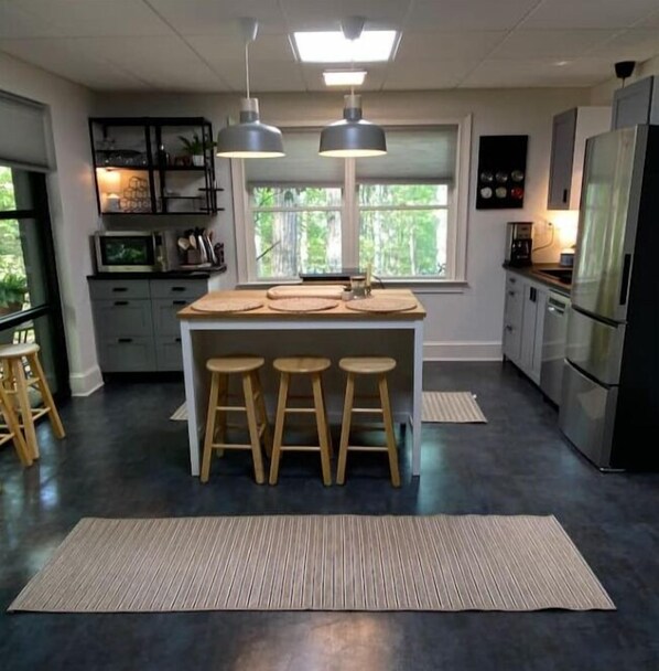 A modern kitchen with a central island, bar stools, and a large window providing natural light. - Trilith Studios Area Lakefront (Sharpsburg)