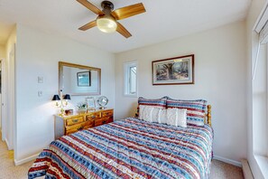 Un dormitorio con una cama de madera, un ventilador de techo, un aparador y un cuadro en la pared.
