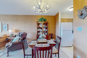 A dining area with a wooden table, chairs, a chandelier, a cabinet with glass doors, and a refrigerator.