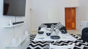 A modern living room with a flat-screen TV mounted on the wall, a dining table set with plates, bowls, and cutlery, and a black and white chevron-patterned rug. - Angel's house in Sorrento coast (Meta)