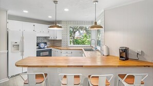 Una cocina moderna con armarios blancos, encimera de madera y luces colgantes.