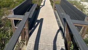 Una pasarela de madera que lleva a una playa bajo un cielo azul despejado.
