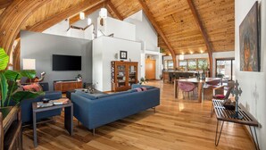 A spacious living area with a high wooden ceiling, a blue sofa, a wooden dining table, and a kitchen in the background. - Stunning Repurposed Church, lofted, pet friendly, Free Botanic Garden admit 6 (Denver)