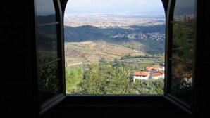 A view through a window with an arched frame, overlooking a valley with scattered buildings and greenery. - Podere Belvedere - Superbe et Grande Villa de Campagne Avec Piscine Privée (Carmignano)