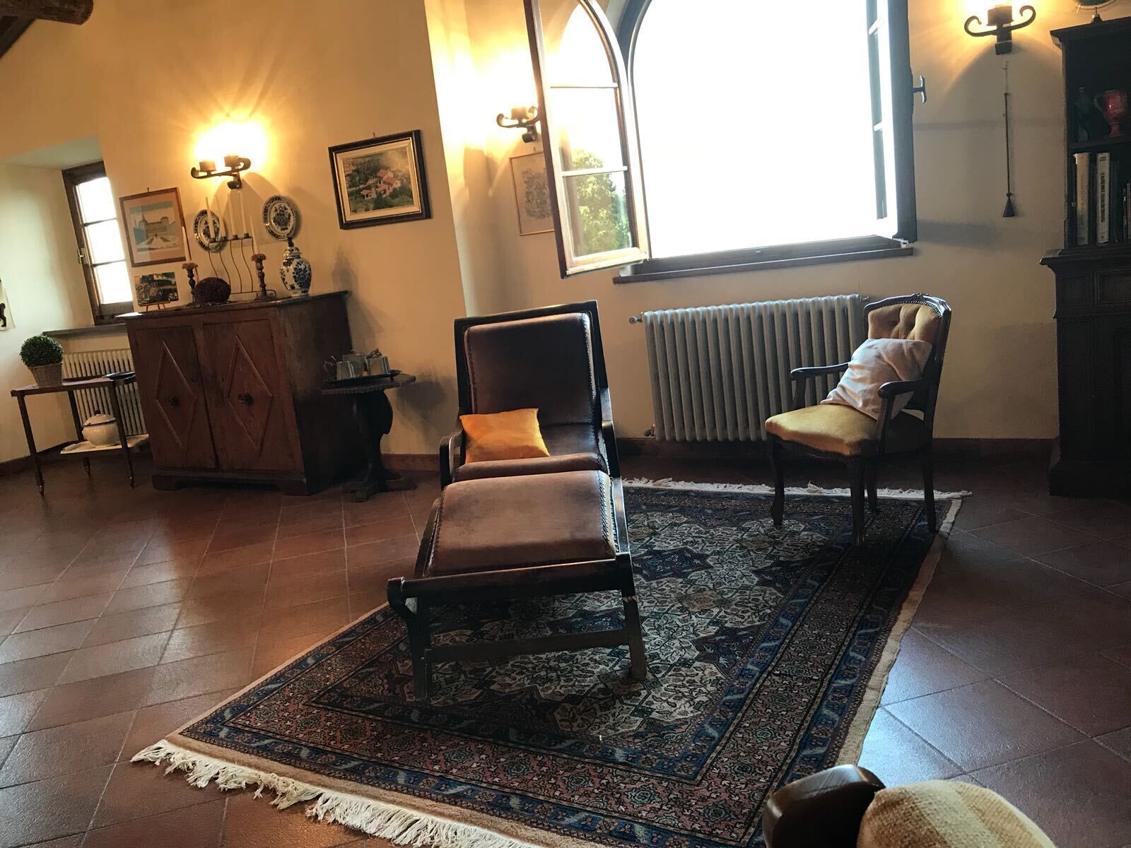 Un salón con un sofá de cuero marrón, una alfombra estampada, un mueble de madera y un radiador.