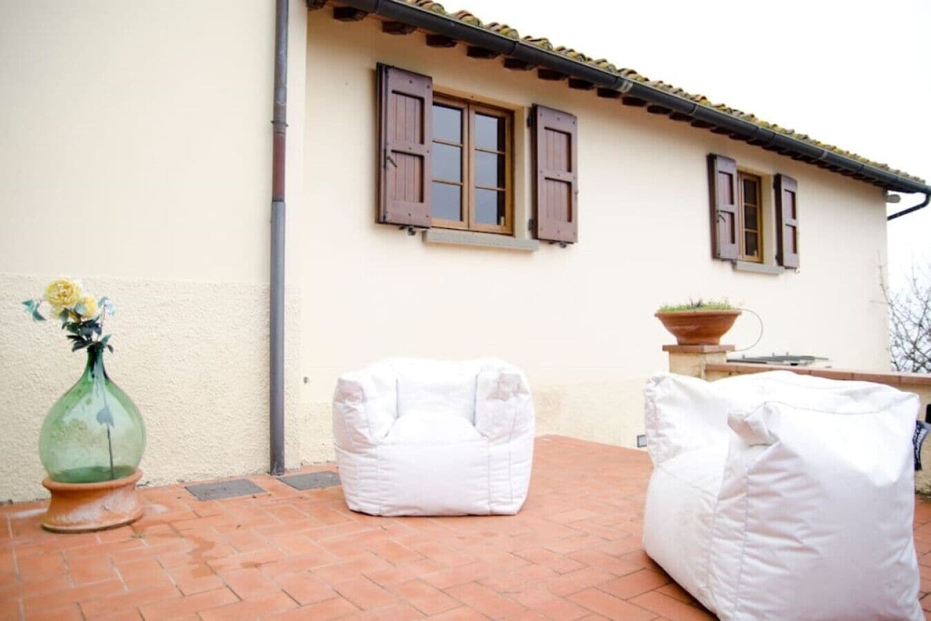 A patio with two white bean bags and a green vase with flowers.