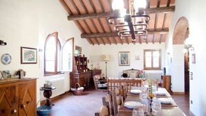 A dining area with a long wooden table set for a meal, a chandelier, and a rustic ceiling. - Podere Belvedere - Superbe et Grande Villa de Campagne Avec Piscine Privée (Carmignano)