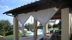 A covered outdoor seating area with a pool in the background. - Podere Belvedere - Superbe et Grande Villa de Campagne Avec Piscine Privée (Carmignano)