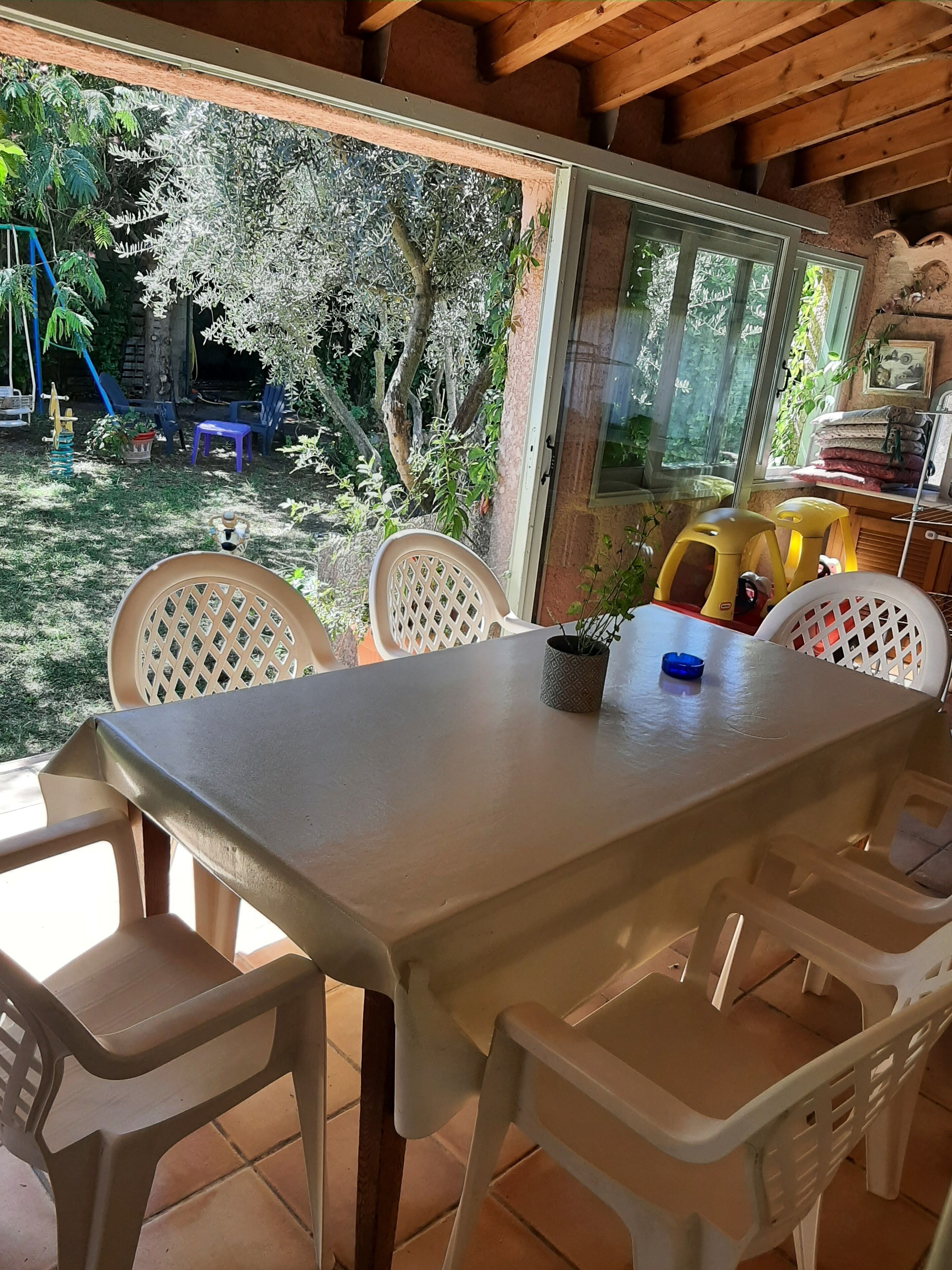 A covered patio with a table and chairs, a view of the garden, and a wooden ceiling.