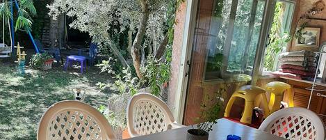 A covered patio with a table and chairs, a view of the garden, and a wooden ceiling.
