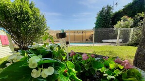 Un jardín con diversas plantas y flores, un área cercada y un edificio al fondo.