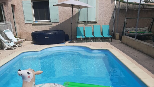 Una piscina con juguetes inflables, una zona de descanso con sillas y un edificio con persianas.