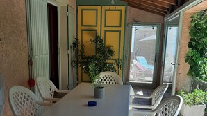 Un patio techado con mesa y sillas, un ventilador de techo y vistas a un parque infantil colorido.