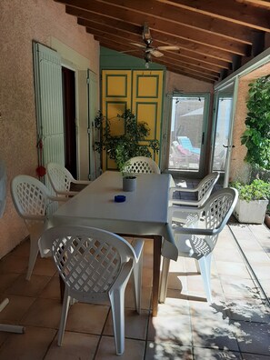 Un portico coperto con tavolo e sedie, una ventola a soffitto e vista su un'area giochi colorata.
