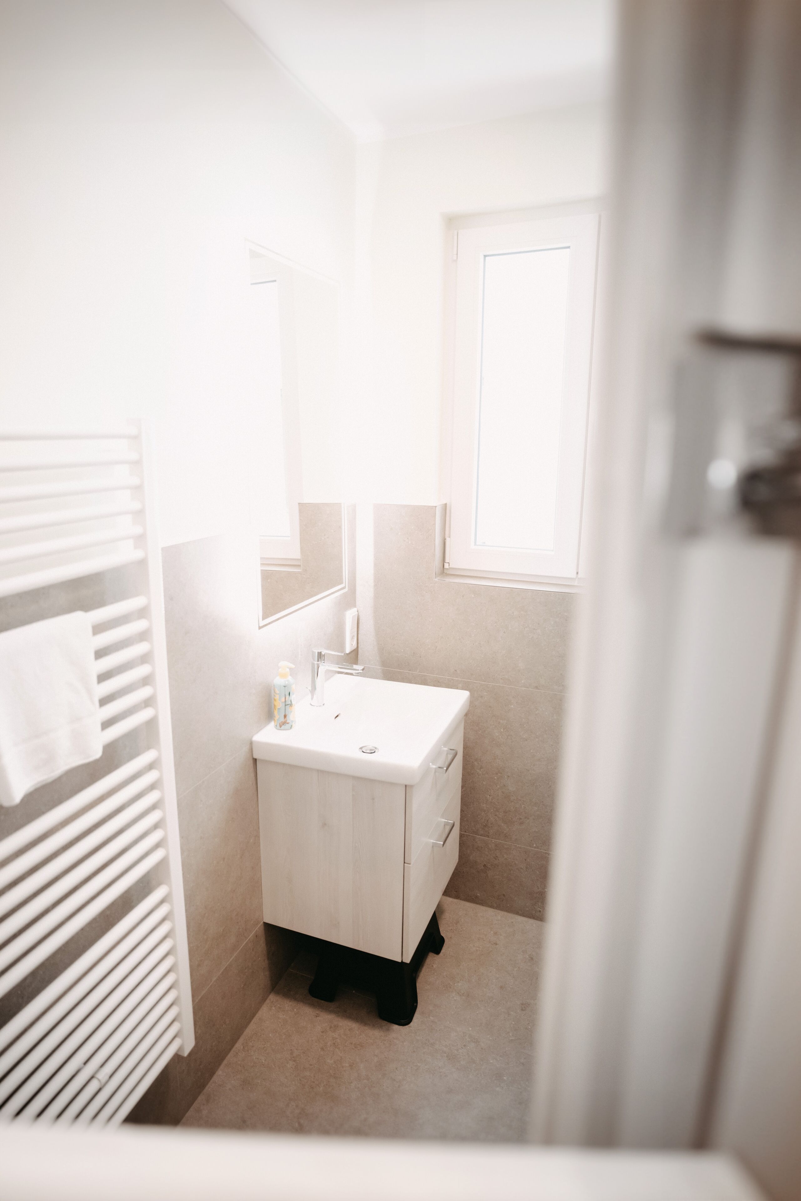 A small, bright bathroom with a white sink, a mirror, and a towel rack.