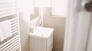 A small, bright bathroom with a white sink, a mirror, and a towel rack.