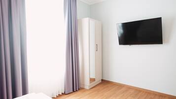 Una habitación con cama, armario, televisor en la pared y ventana con cortinas.