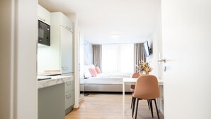 A modern kitchen with built-in appliances, a dining area with a white table and chairs, and a window with curtains. - House of Blooms (Fulda)