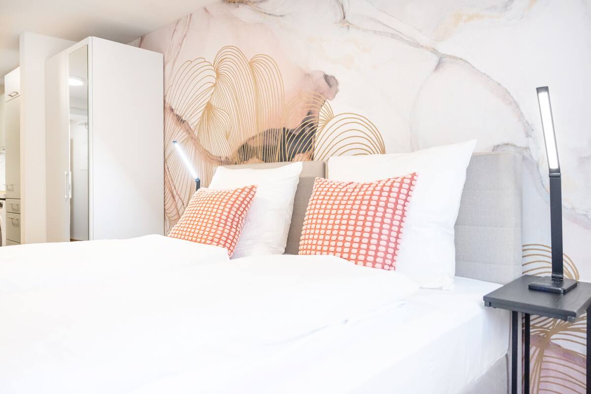 A modern hotel room with a bed, white bedding, and a decorative wall mural.