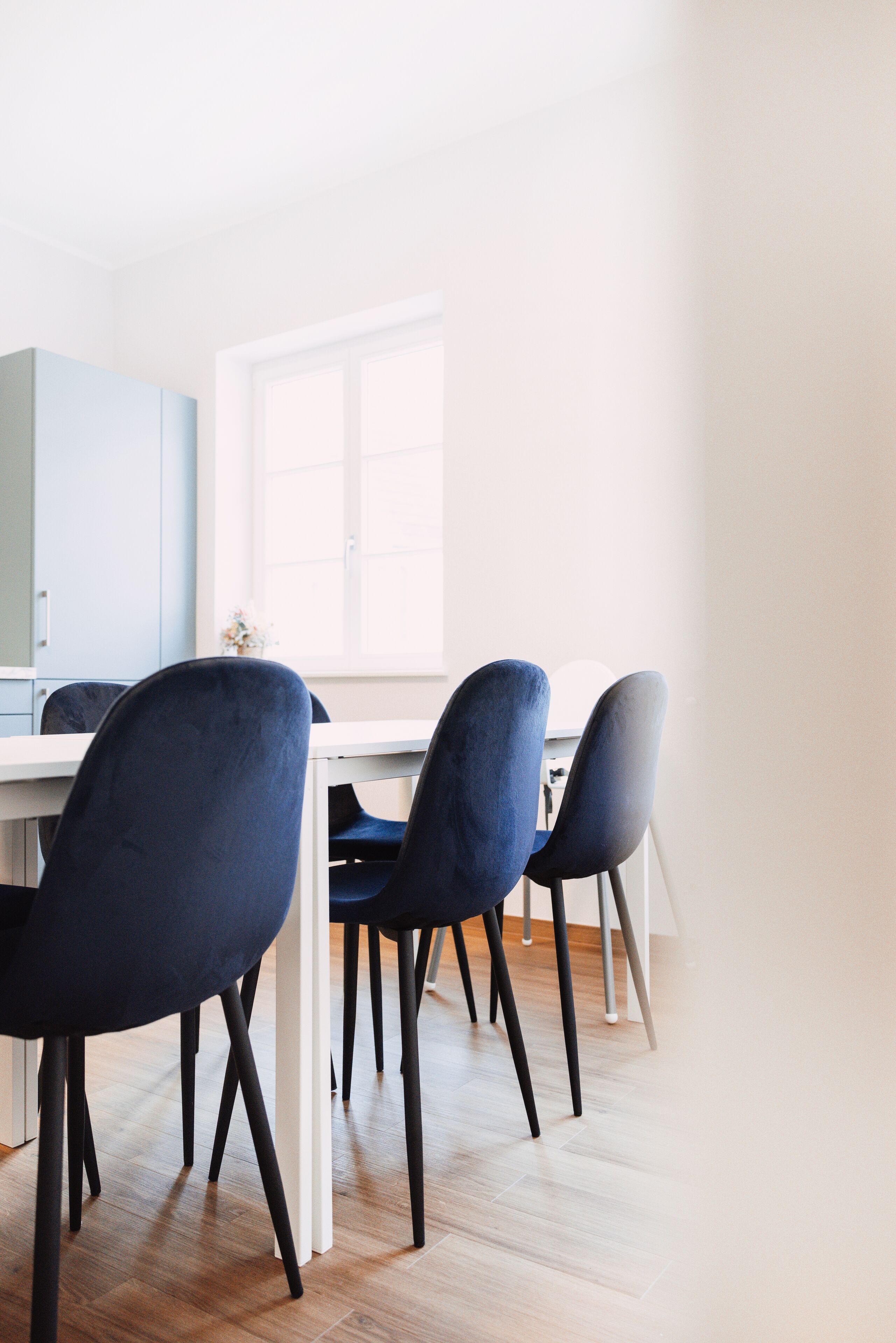 Een moderne keuken met een wit aanrecht, donkerblauwe stoelen en een lichtblauwe kast.
