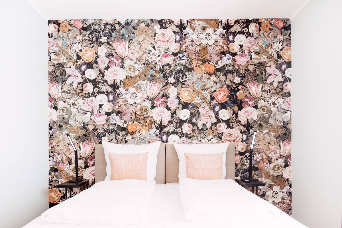 A bedroom with a floral wallpaper, two bedside tables, and a bed with white bedding.