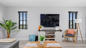 A modern living room with a grey sofa, a wooden coffee table, a TV, and a wicker chair. - Casa Rockport - Waterfront + Pet Friendly
 (Rockport)
