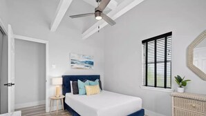 A bedroom with a bed, a ceiling fan, a window with blinds, a bedside table with a lamp, and a wall-mounted mirror. - Casa Rockport - Waterfront + Pet Friendly
 (Rockport)